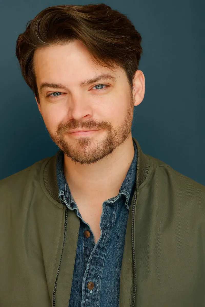 Andrew Russell warm on-camera headshot in a green jacket and denim shirt
