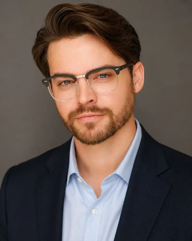 Andrew Russell on-camera headshot in a navy suit and glasses